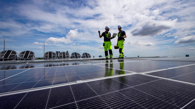Workers install solar panels on a building rooftop under a clear blue sky