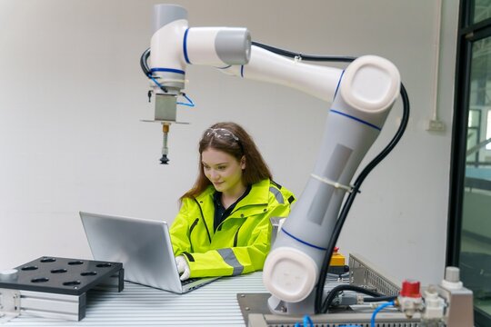Technician interacts with robotic arm while working on a laptop in a laboratory setting - Powered by Adobe