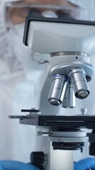 Close up of medical virologist in a hazmat suit, mask, and gloves, diligently working at a microscope in a laboratory researching viruses. Medicine and science concept