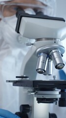 Close up of medical virologist in a hazmat suit, mask, and gloves, diligently working at a microscope in a laboratory researching viruses. Medicine and science concept