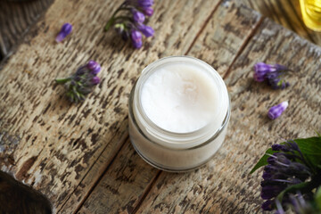 A jar of homemade comfrey root ointment with fresh blooming symphytum plant