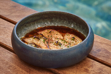 Deliciously Seasoned Fish Dish with Accompanying Sauce Served in a Rustic Bowl by a Tranquil Poolside Setting, Perfect for Culinary Enthusiasts