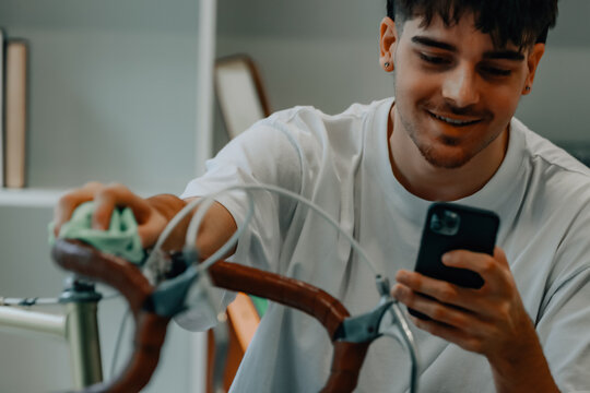 young man cleaning or preparing vintage bicycle looking at mobile phone or app