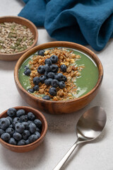 Healthy Green Smoothie Bowl with Granola and Blueberries in Wooden Bowl on White Background