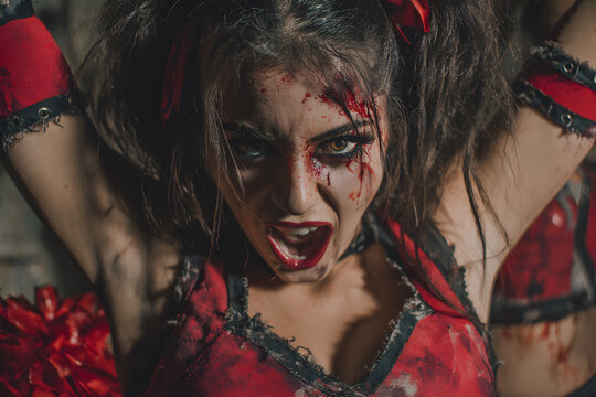 Haunting Halloween Night: Zombie Cheerleader Strikes a Spooky Pose in Tattered Red and Black Ensemble with Creepy Cheer and Eerie Atmosphere!