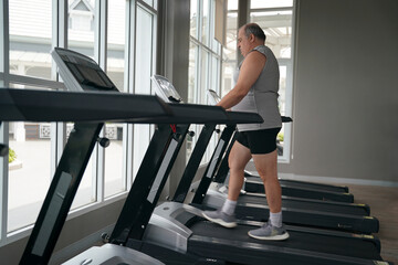 Fototapeta premium Man exercising on treadmill in bright fitness center during daytime