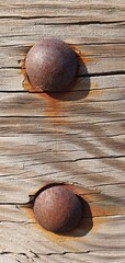 Close-up of two rusty bolts on weathered wooden planks, showing natural cracks, grain, and oxidized metal texture with warm tones of rust against aged timber
