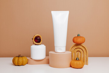 Tube of body lotion and facial cream container on brown podium with autumn decoration and pumpkins, dry skin care, moisturizer mockup containers
