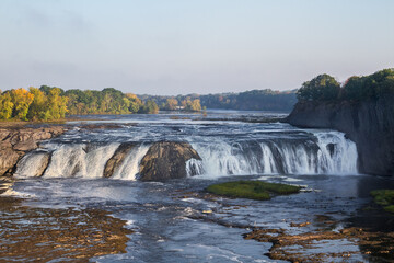 Expansive Waterfall Cascading Over Rocky Ledge with Autumn Foliage in the Distance