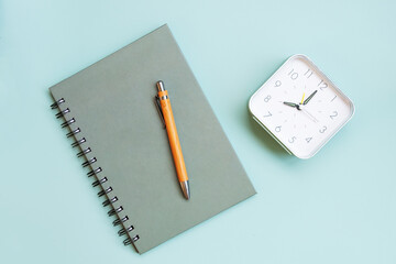 Green spiral notebook, wooden pen and clock on lightblue Background. Copy space. Business, school.