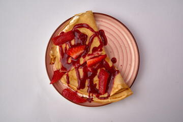 Deliciously Crafted Crepe Topped with Fresh Strawberries and Drizzled with Rich Strawberry Sauce on a Decorative Plate
