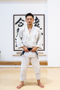 Asian martial arts athlete wearing keikogi and black belt posing in dojo
