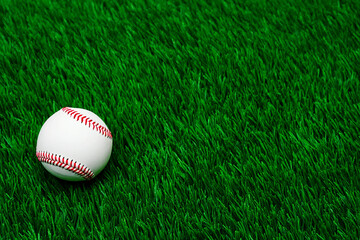 White baseball resting on vibrant green artificial turf stitching