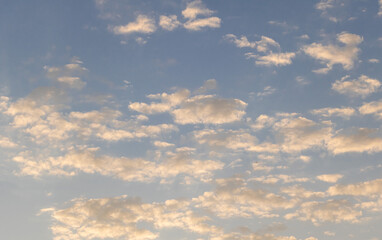 Obraz premium Golden-hued clouds scattered across a soft blue sky during sunrise or sunset