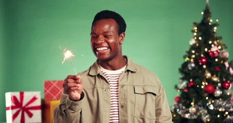 Man, sparkler and celebration with Christmas tree in studio, excited and laugh on green background. African person, fireworks and happy with present, gift and party with festive holiday at xmas