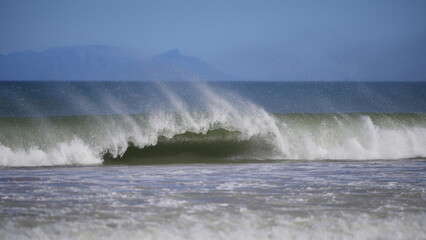 Powerful ocean wave crashing on shore under clear blue sky