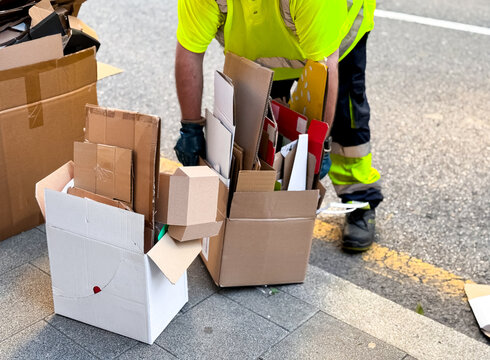 Worker collecting cardboard boxes for recycling on street