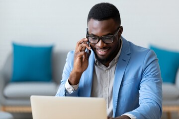 Smiling African American Man on Phone with Laptop on His Lap, Working From Home