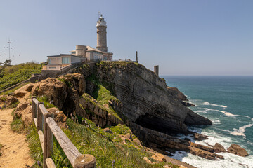Obraz premium Santander, Spain. Sunny day view of Cabo Mayor Lighthouse perched on cliffs above the Bay of Biscay, with rocky coast and sea surrounding the ash-stone cylindrical tower