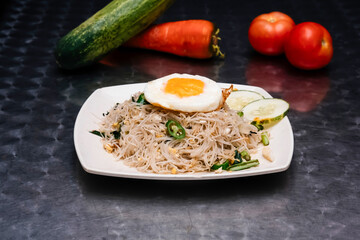 Chicken Mee Hoon Goreng with a Fried Egg and Fresh Cucumber Slices on a Plate isolated on dark background side view of Malaysian food