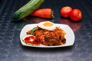 Spicy Mutton Mee Hoon Goreng with Fried Egg, Cucumber, and Tomato in plate isolated on dark background side view of Malaysian food