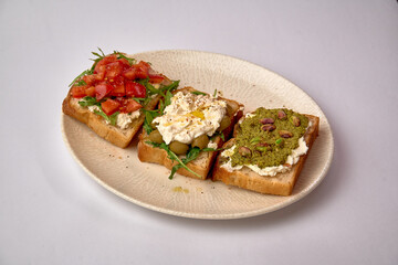 A Colorful Trio of Gourmet Toasts Featuring Fresh Tomatoes, Creamy Cheese, and Nutty Pesto on Artisan Bread Served on a Ceramic Plate