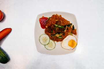 Spicy Mutton Nasi Goreng with Fried Egg, Cucumber Slices, and Chili Garnishes on a Plate isolated on white background top view of Malaysian food