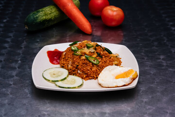 Spicy Chicken Nasi Goreng with Fried Egg, Cucumber Slices, and Chili Sauce in plate isolated on dark background side view of Malaysian food