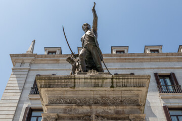 Santander, Spain. Full view of the bronze statue of Captain Pedro Velarde on a stone pedestal at the entrance to Plaza Porticada, with Neoclassical portico and surrounding arcaded buildings