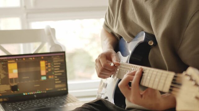 Musician playing electric guitar and recording music in a cozy home studio, working with digital audio workstation (DAW) on laptop. Perfect for themes of music production, songwriting, composing