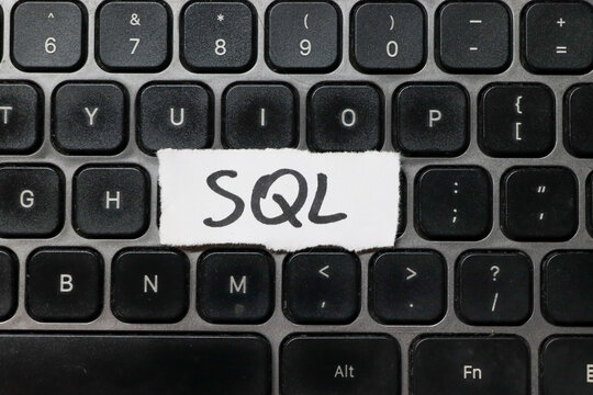 Handwritten SQL on a white paper strip placed on a modern black keyboard. This image symbolizes programming, database management, and coding practices in technology.