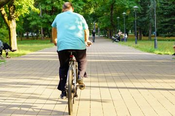Fototapeta premium Man cycling on paved path in park under sunlight with lush trees around during afternoon