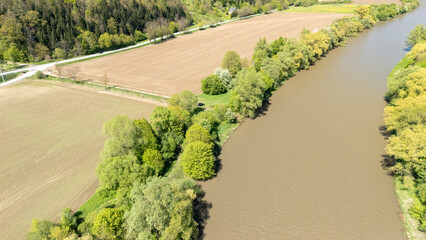 Aerial view of a serene river flowing through fertile fields surrounded by lush green trees. This tranquil landscape captures the beauty of nature in spring.
