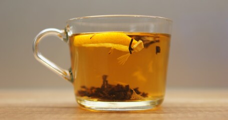 Transparent mug filled with herbal tea and fresh lemon slice on surface put on wooden table. Aromatic beverage with rich taste for morning relaxation