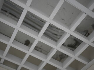 Close-up of a suspended grid ceiling with exposed electrical conduit pipes on a concrete surface

