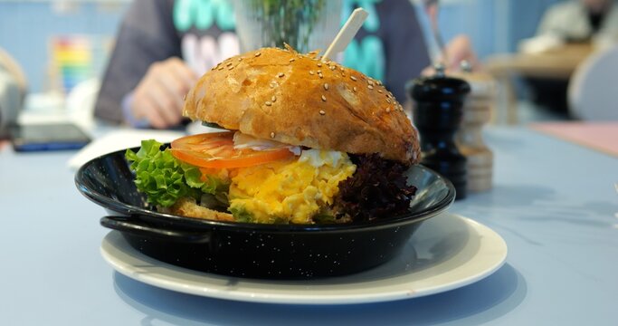 Burger features scrambled egg on table against visitor eating in restaurant. Ingredients sandwiched between toasted sesame seed bun haves exuding nutty aroma - Powered by Adobe