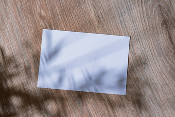 Minimalistic white mockup of a blank postcard lying on a wooden surface with soft natural shadows...