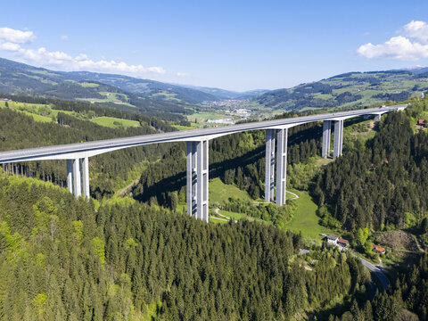 Aerial view of a towering viaduct slicing through verdant, tree-covered hills under a clear sky, Lavanttal, Wolfsberg, Carinthia, Austria.