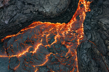 Aerial view of fiery lava snaking through the dark, jagged landscape, a stark contrast of heat and stone, Reykjanes, GrindavÃ­kurbÃ¦r, Iceland.