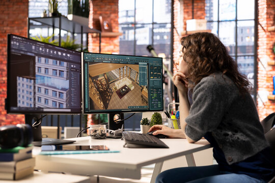 Professional architectural designer configures a floor plan on dual monitors, utilizing computer aided design tools. Woman uses software for digital rendering and interior decoration remodeling.