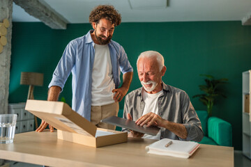 Senior man unboxing new laptop with son at home