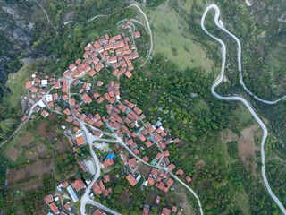 Drone capture of a serene mountain village in Gelemiç, Turkey, displaying winding roads, forested terrain, farmland, and traditional red-roof houses spread across the hills.
