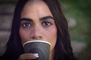 Close up portrait of a young latin woman drinking coffee from a disposable cup in a natural setting