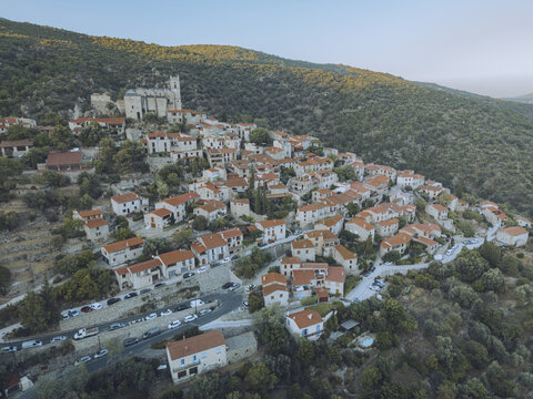 Aerial view of sunlit rooftops cascade down the hillside towards the winding roads, with the ancient castle standing guard atop the village, Eus, Pyr&Atilde;&copy;n&Atilde;&copy;es-Orientales, France.