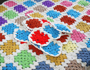 Colorful handmade crocheted granny squares laying on surface of completed blanket that has been put together after joining the many squares