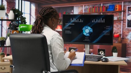 Student doing academic research on internet to gain financial knowledge useful for career development, taking notes. African american woman in online class doing courses, writing down info, camera B