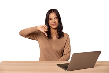 Filipino woman at desk with laptop showing a dislike gesture, thumbs down. Disagreement concept.