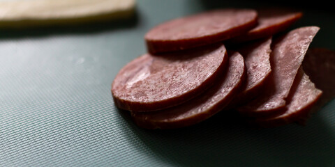 Pieces of sausage and a piece of cheese lie on a blue cutting board. The pieces of sausage are a rich red color with a marbled layer of fat. A rustic contrast to the modern look of the board.