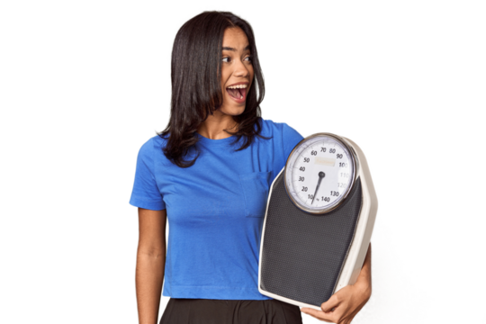 Filipino woman with scale in studio points with thumb finger away, laughing and carefree.