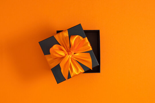 Elegant half-open black gift box with orange ribbon on orange background. - Powered by Adobe